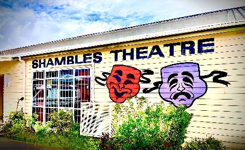 External view of the Shambles Theatre in Rotorua. This is a wooden building, distinguished by the masks of tragedy (purple) and comedy (red) painted on the entrance wall.